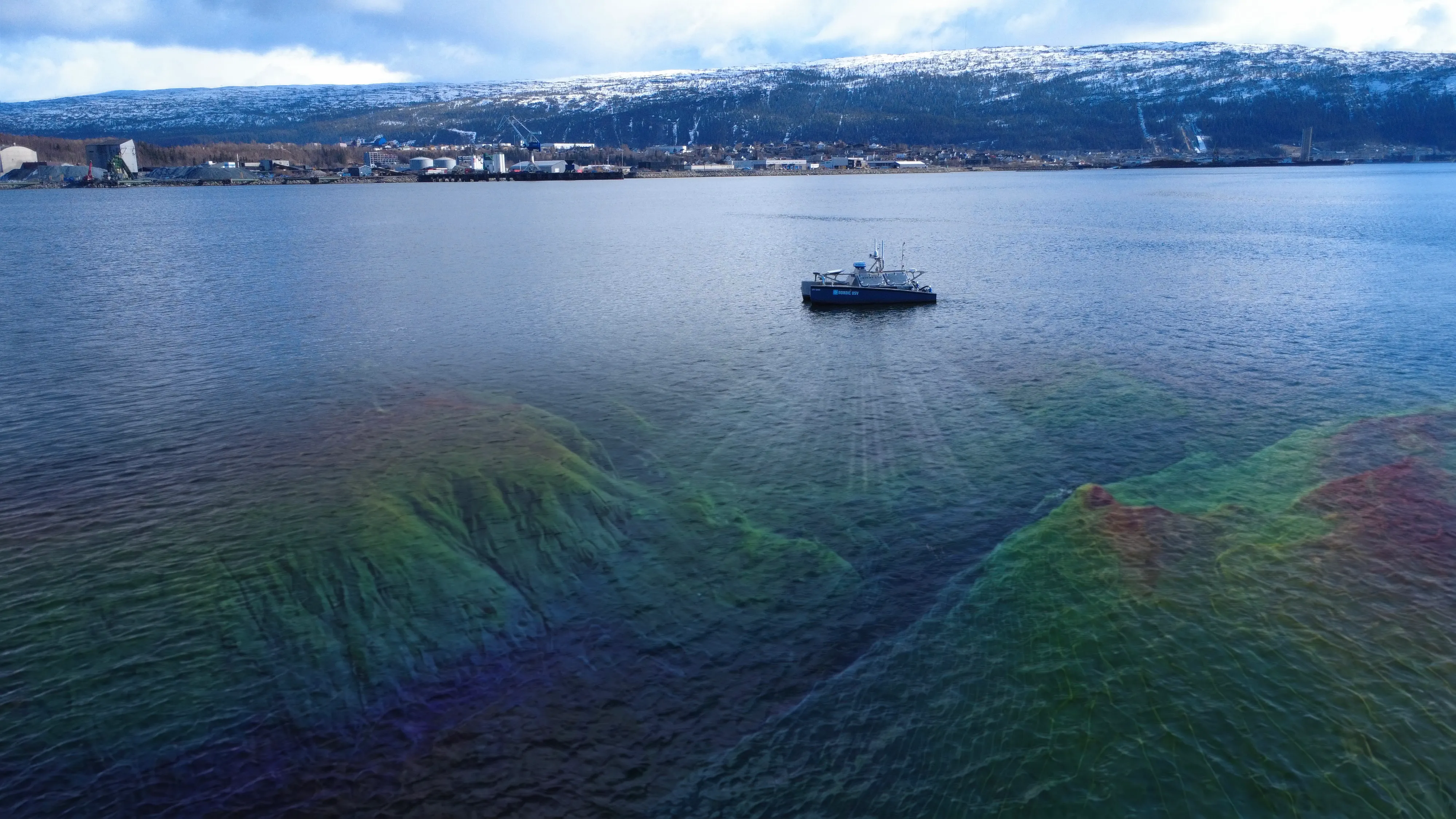 Ubemannet båt i en fjord som kartlegger havbunnen med multistråleekkolodd. Under vannflaten vises sjøbunnen som en fargelagt 3D-modell.